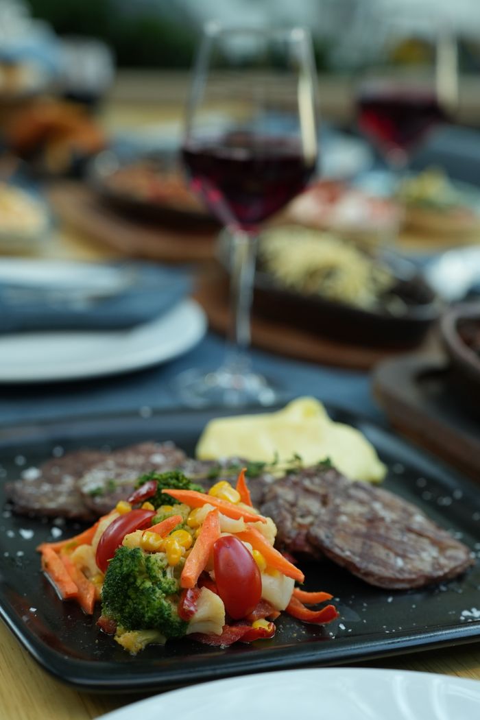 A gourmet meal featuring steak and vegetables paired with red wine on an elegant table setting.